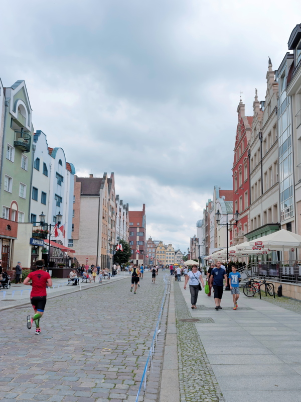 14 - A cobblestone street in the Old Town of Elbląg, Poland, lined with reconstructed historic-style buildings and people walking or running